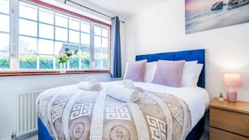 A hotel room with a large bed, a window with curtains, a bedside table with a lamp, and a painting on the wall.