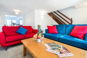 Ein Wohnzimmer mit einem roten und blauen Sofagarnitur, einem Holztisch und einer Obstschale.