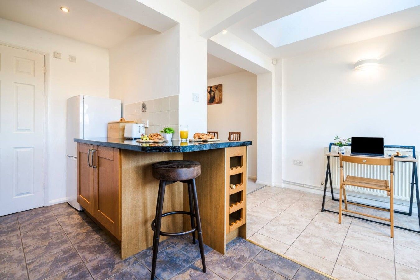 Una cocina con barra, refrigerador, tostadora y una computadora portátil sobre una mesa.