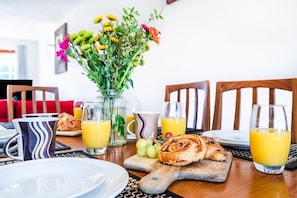 Una escena de desayuno con una mesa, platos, vasos de jugo de naranja, un florero con flores y un pastel sobre una tabla de cortar.