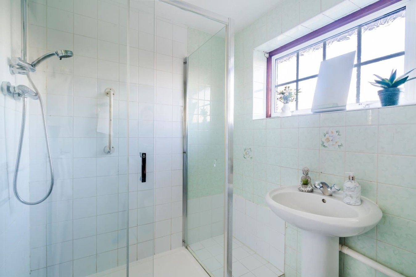 A bathroom with a glass-enclosed shower, a white sink, and a window with a view.