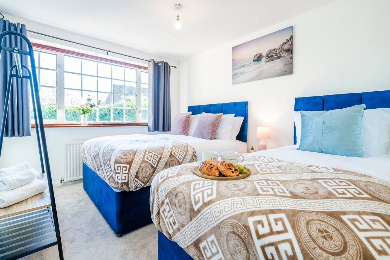 A hotel room with two beds, a window with curtains, a painting on the wall, and a breakfast tray on the bed.
