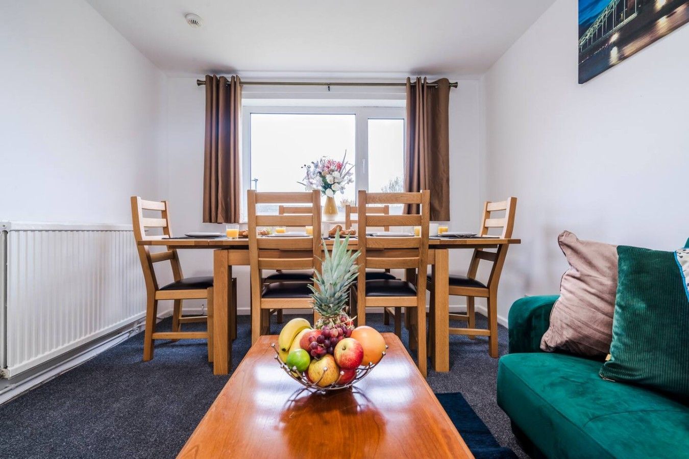 A dining area with a wooden table, chairs, and a fruit bowl.