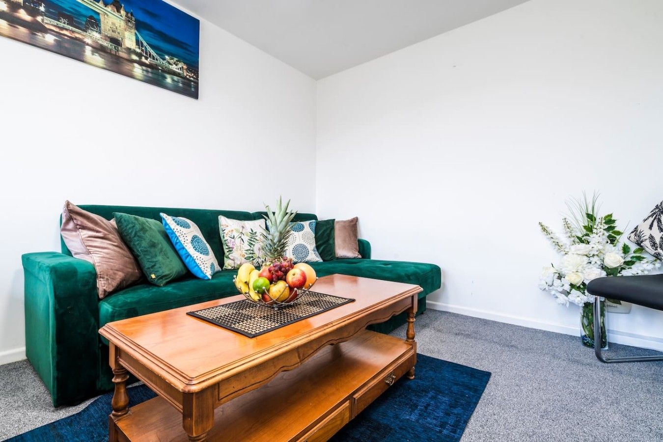 A living room with a green sofa, a wooden coffee table with fruit, and a painting on the wall.