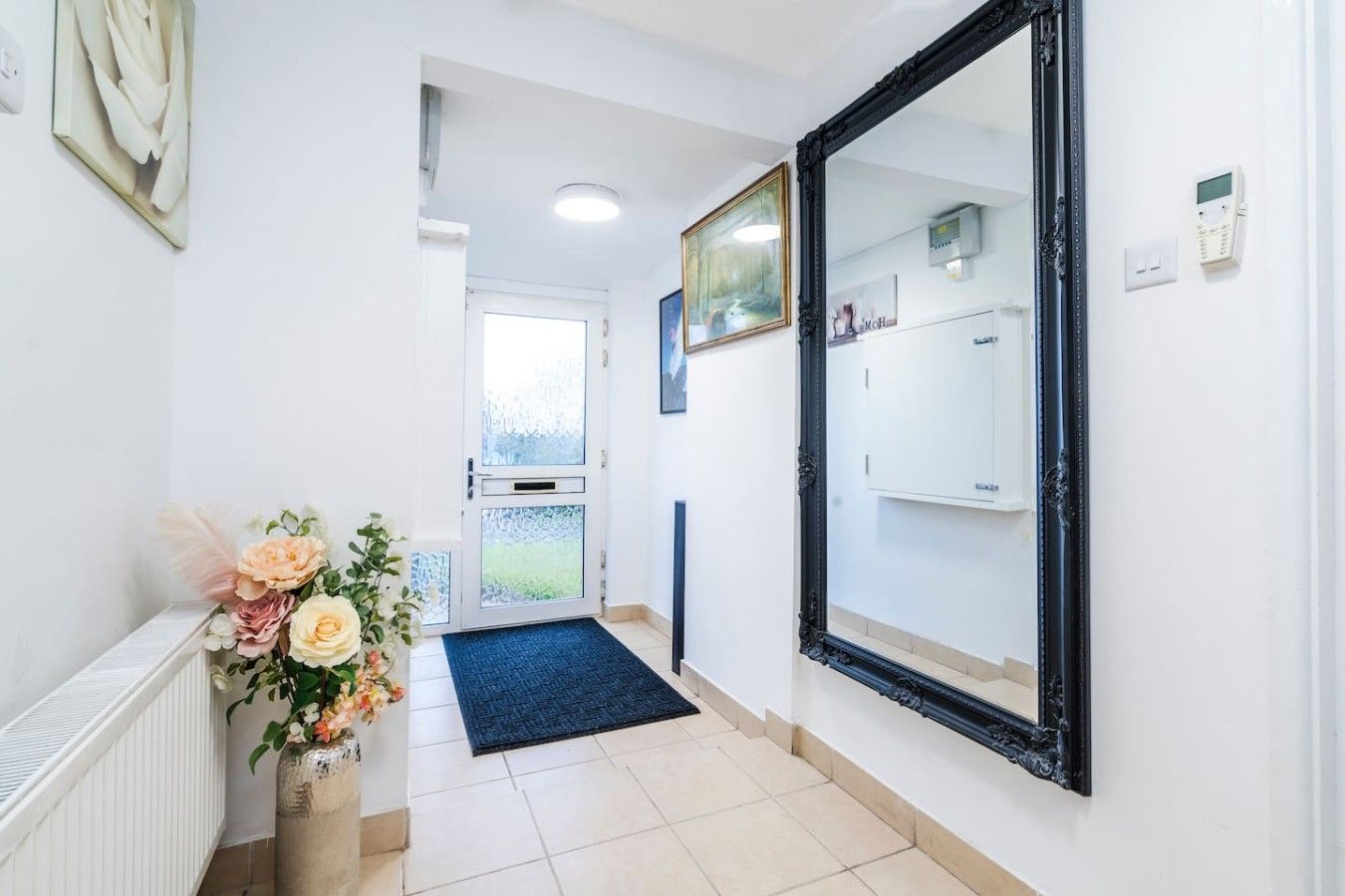 A hallway with a large mirror, a door with frosted glass, a radiator, and a vase with flowers.