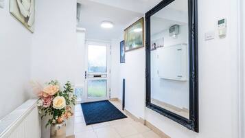 A hallway with a large mirror, a door with frosted glass, a radiator, and a vase with flowers.
