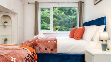 Un dormitorio con cama, mesita de noche, ventana con cortinas, una planta y una estantería con una planta.