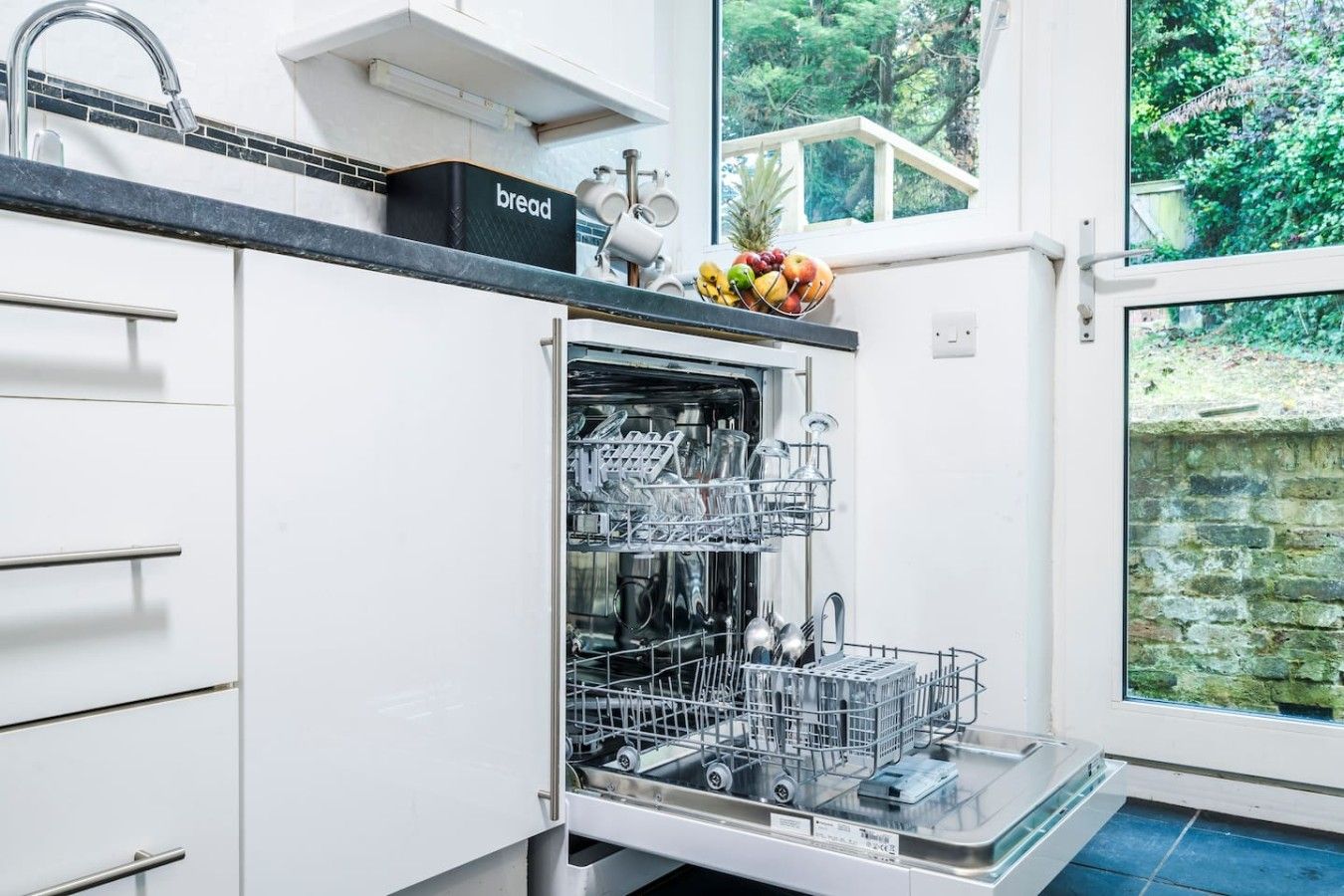 A kitchen with a built-in dishwasher, a bread box, and a fruit bowl on the counter.