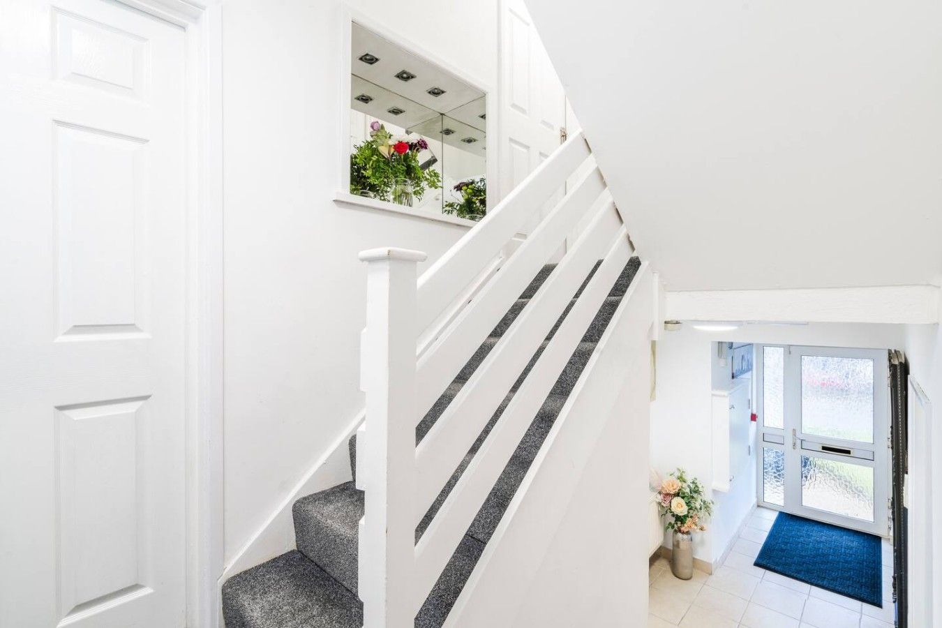 A white interior staircase with a glass railing, leading to a landing with a door and a window.