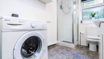 A modern bathroom with a washing machine, a glass shower enclosure, and a toilet.