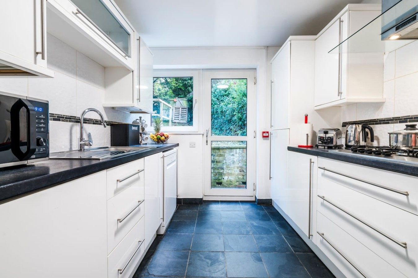 A modern kitchen with white cabinetry, a black countertop, and a view to the outside.