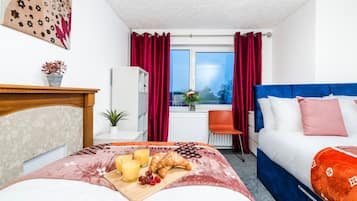 Habitación de hotel con cama, sofá, ventana con cortinas, una mesita con provisiones para el desayuno y vistas al exterior.