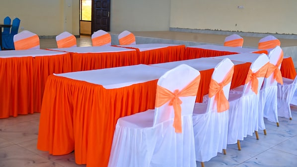 A conference room with tables covered in white tablecloths and orange chair covers, arranged in rows.
