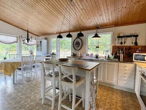 A kitchen with wooden ceiling, white cabinets, a dining area with white chairs, and a view of greenery outside. - 6 Person Holiday Home in Figeholm (Figeholm)