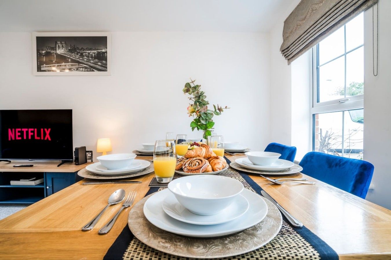 A dining area with a table set for breakfast, a television displaying 'NETFLIX', and a window with a view.