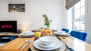 A dining area with a table set for breakfast, a television displaying 'NETFLIX', and a window with a view.