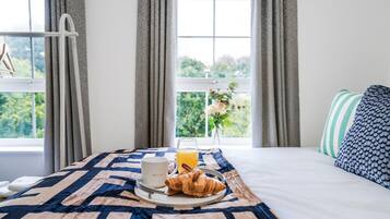 A hotel room with a bed, a breakfast tray with croissants, a mug, and a glass of orange juice.