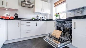Una cocina moderna con armarios blancos, extractor de acero inoxidable y lavavajillas con tabla de cortar en su interior.