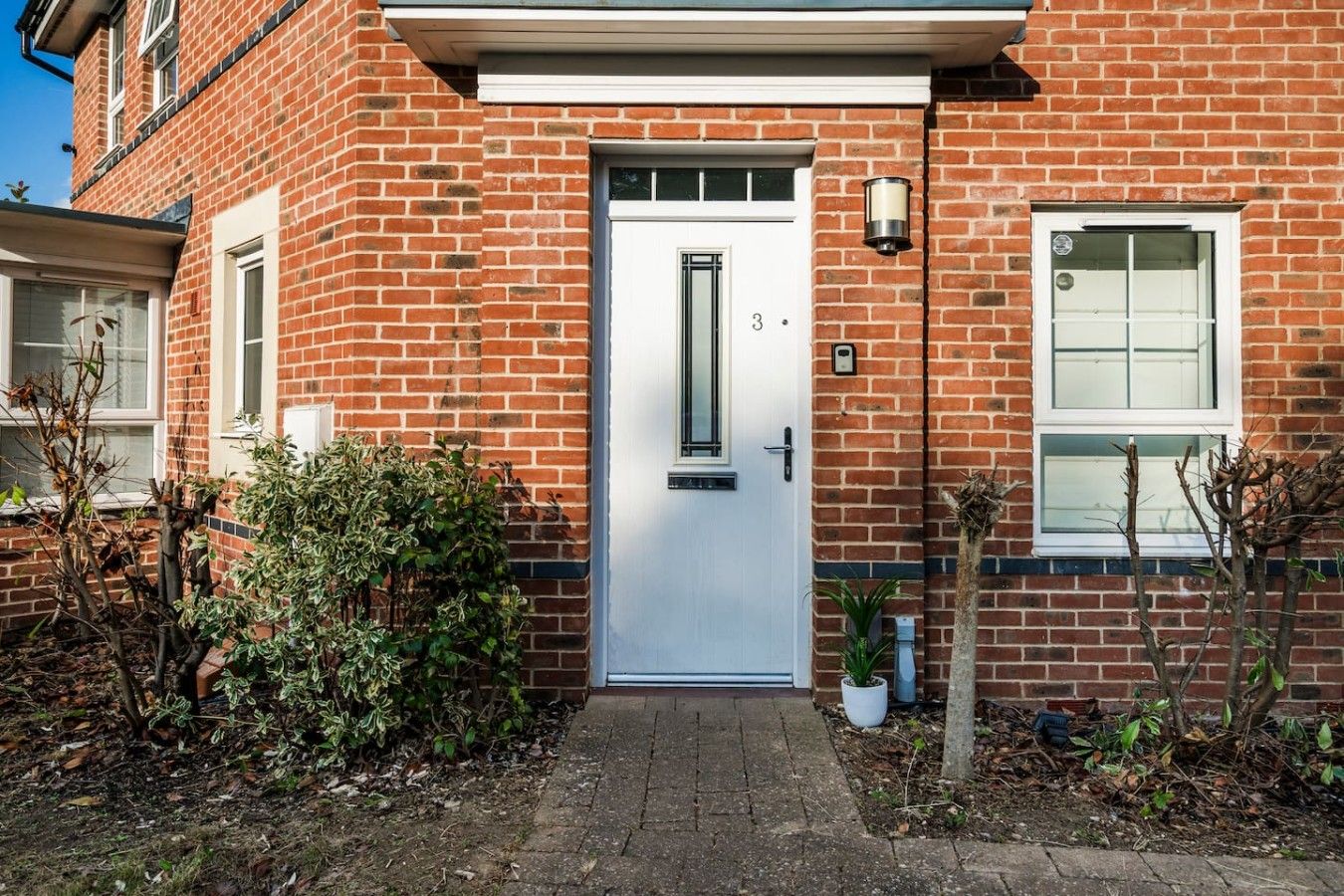 A red brick house with a white door, a small garden, and a potted plant.
