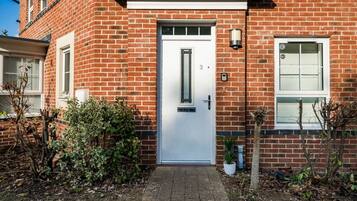 A red brick house with a white door, a small garden, and a potted plant.