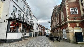 Una calle empedrada flanqueada por edificios históricos, incluyendo un pub con un letrero que dice 'Old Bell'.