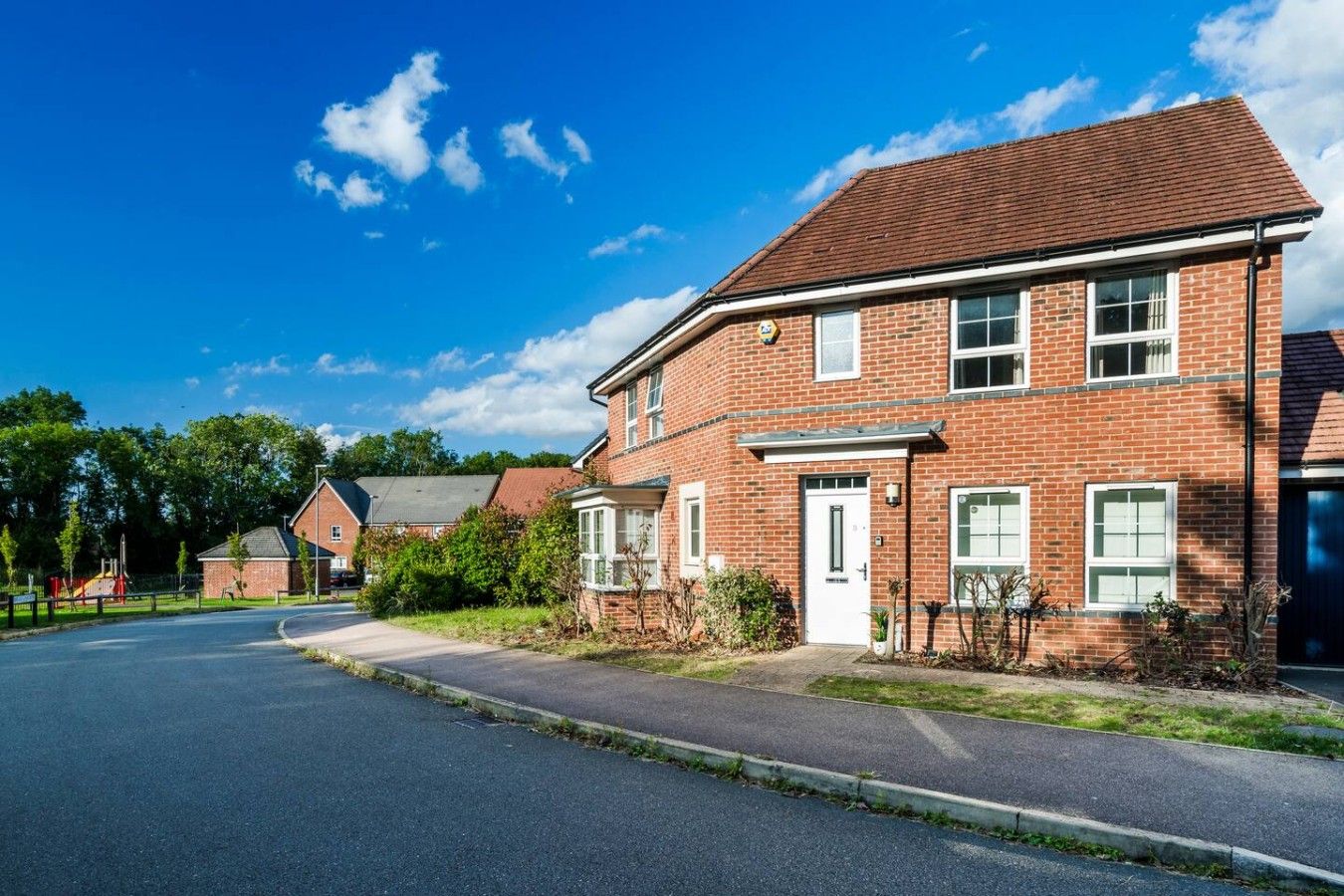 A two-story brick house with a front door and windows, a driveway, and a clear blue sky.