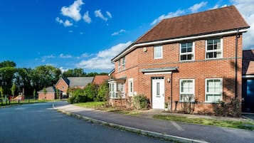 A two-story brick house with a front door and windows, a driveway, and a clear blue sky.