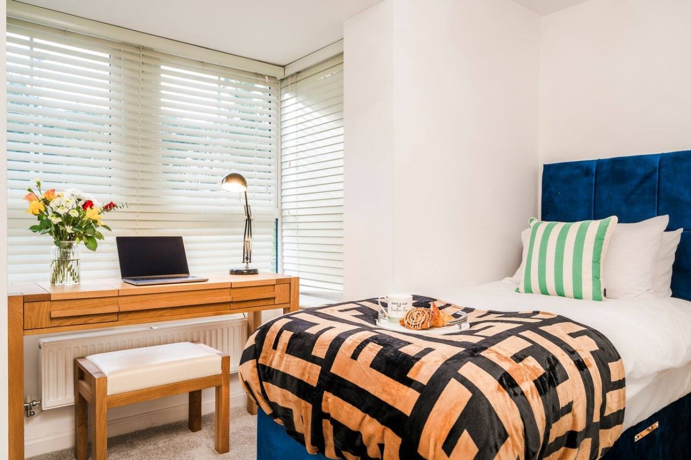 A bedroom with a bed, a desk with a laptop, a chair, and a radiator.