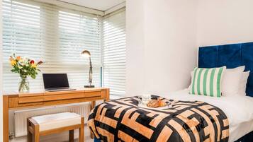 A bedroom with a bed, a desk with a laptop, a chair, and a radiator.