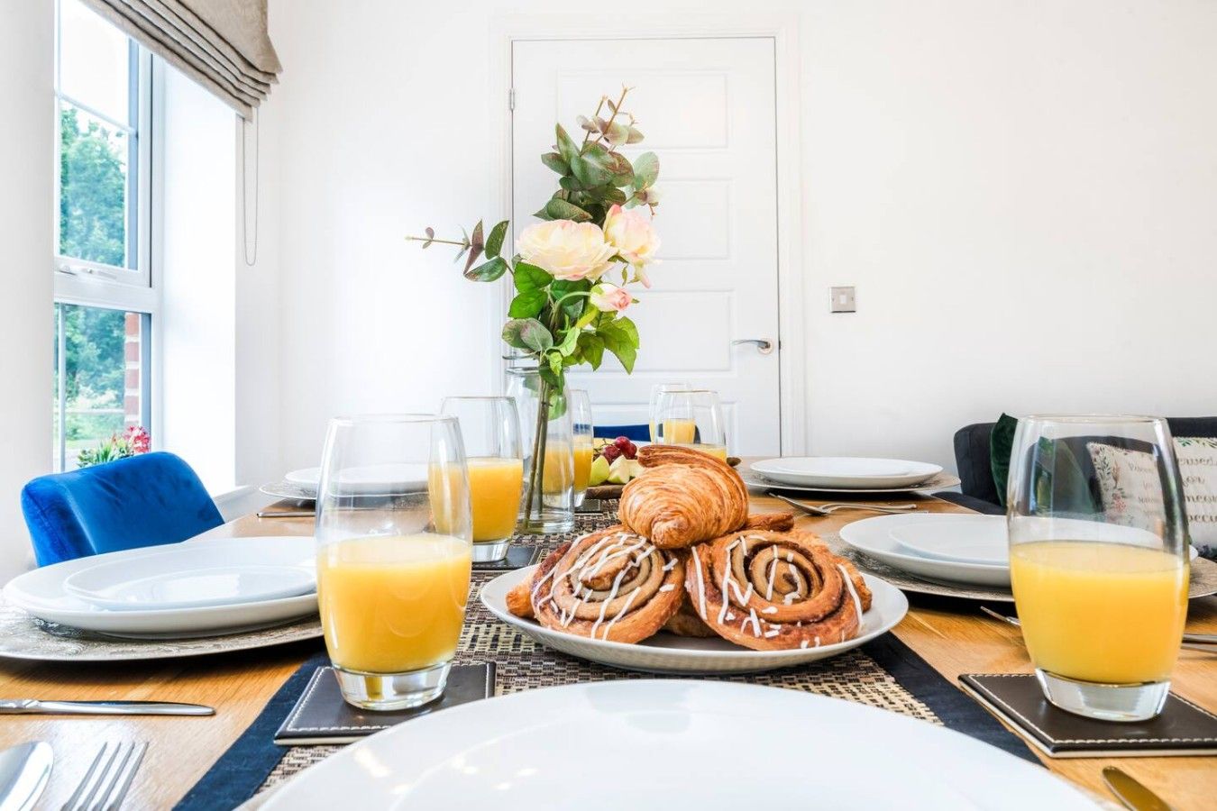 Una colazione servita con piatti di cibo, bicchieri di succo d'arancia e un vaso con fiori.