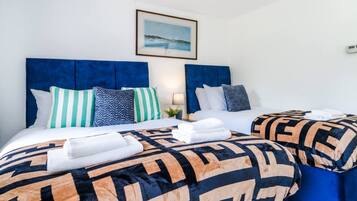 Habitación de hotel con dos camas, cada una con cabecero azul, ropa de cama blanca y almohadones estampados. Encima de las camas hay un cuadro en la pared.