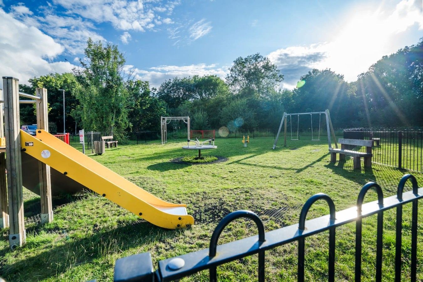 A playground with a yellow slide, swings, and a fenced area.