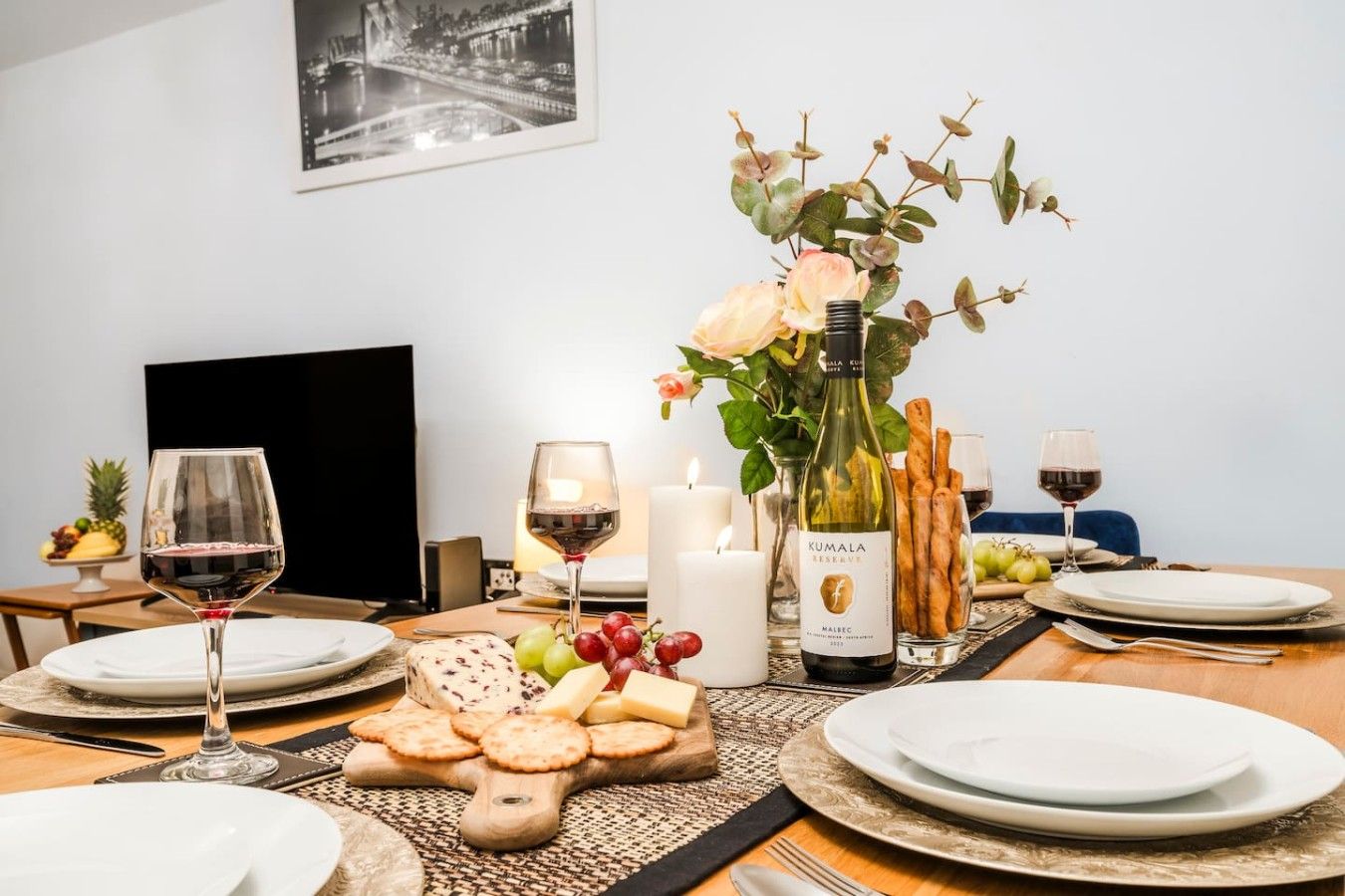 Ett dukat matbord med tallrikar, glas, en vinflaska, en ostbricka och en vas med blommor.