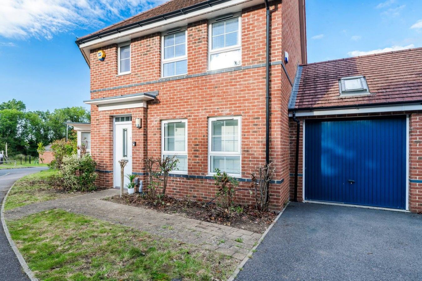 A two-story brick house with a garage, a front door, and a small garden area.