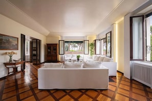 Ein geräumiges Wohnzimmer mit einem großen weißen Sofa, einem Couchtisch und Blick ins Freie durch eine Glastür.