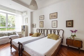 Ein Hotelzimmer mit zwei Betten, einem Fenster mit Vorhängen, einem Nachttisch mit Lampe und gerahmten Bildern an der Wand.
