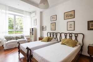 A hotel room with two beds, a sofa, a bookshelf, and framed pictures on the wall. - Aventino Luxury Apartments (Roma)