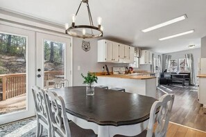 A modern kitchen with white cabinets, a central island, and a dining area with a dark table and white chairs. - Perfect/private location between Gatlinburg/Pigeon Forge on top of the ridge. (Sevierville)