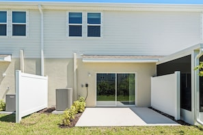 A modern residential building with a covered patio, outdoor air conditioning units, and a sliding glass door entrance. - Seaside Living Venice-Nokomis-Sarasota | 7 MIN TO THE BEACHES | GATED COMMUNITY (Nokomis)
