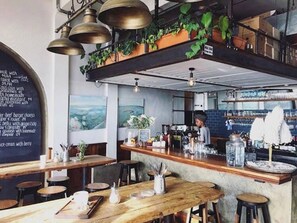 L’intérieur d’un restaurant avec un menu écrit à la craie, des tables en bois, des tabourets de bar et un coin bar avec un barman.