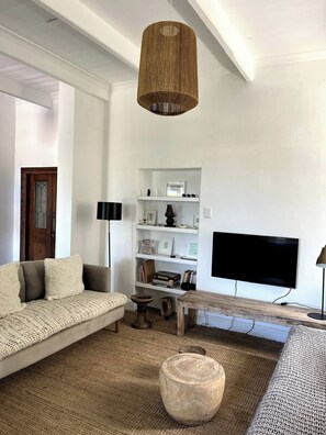 A modern living room with a sofa, a coffee table, a bookshelf, and a television. - The Original Kalk Bay Farmhouse at the Homestead (Cape Town)