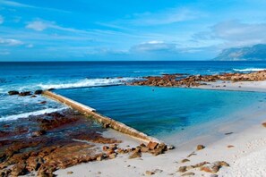 Une plage avec une structure en béton qui s’étend dans l’eau, un rivage rocheux et un ciel bleu clair.