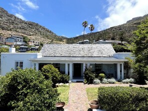 Une maison à deux étages avec une entrée centrale, entourée d’un jardin bien entretenu et dominant un paysage montagneux.