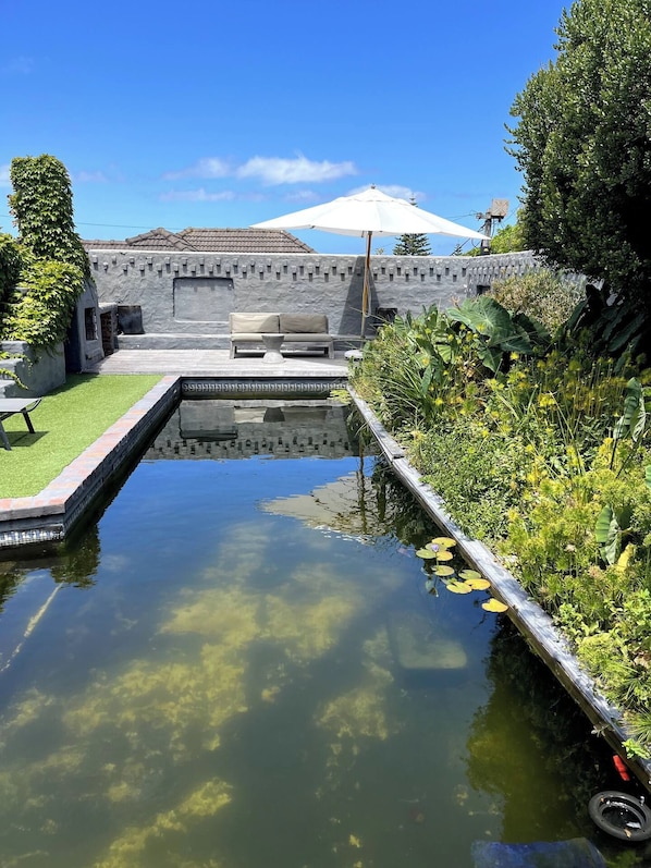 Un espace piscine extérieur paisible, agrémenté d’un mur en pierre, d’un banc et d’une végétation luxuriante.