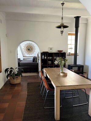 A dining area with a wooden table, chairs, and a vase of flowers. - The Original Kalk Bay Farmhouse at the Homestead (Cape Town)