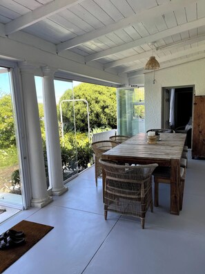 An open-plan living area with a large wooden table, wicker chairs, and a view of greenery outside. - The Original Kalk Bay Farmhouse at the Homestead (Cape Town)