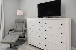 A room with a grey office chair, a white dresser with drawers, and a flat-screen TV on top. - Del Lago - 3 Minutes walk to the Beach (St. Augustine)