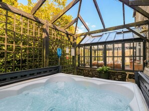 A hot tub inside a greenhouse structure with a view of a garden and a building outside. - Three Mile House (Carnforth)