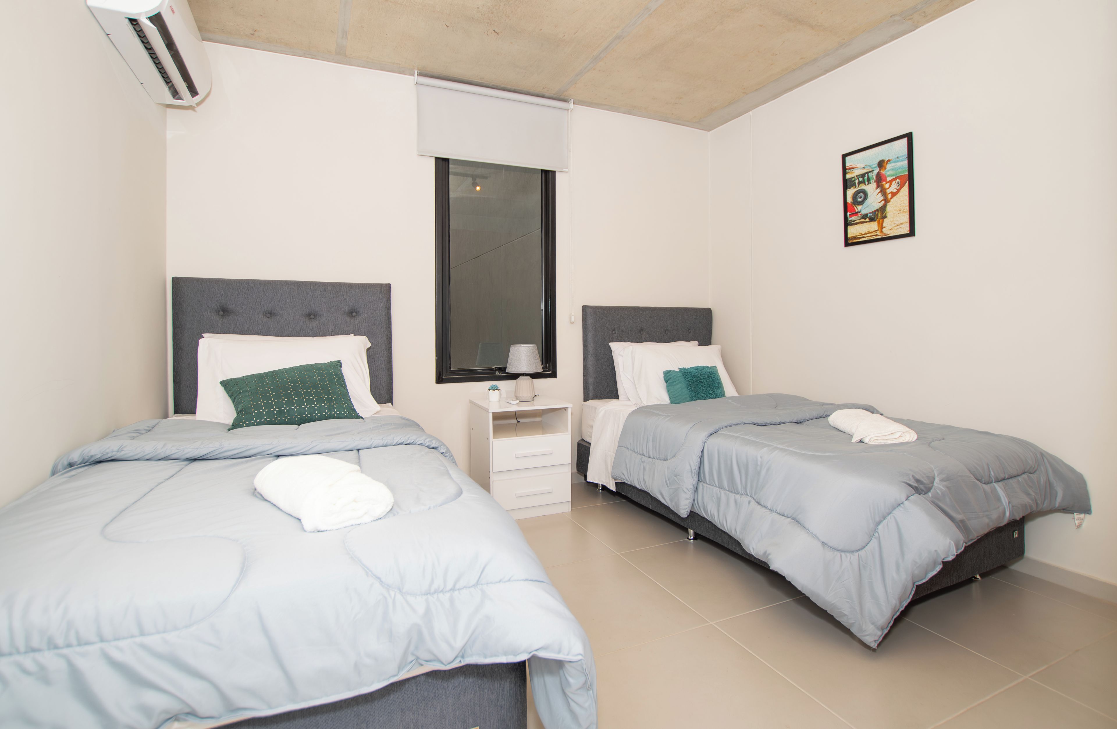 A bedroom with two beds, a nightstand, a mirror, and a wall-mounted picture.
