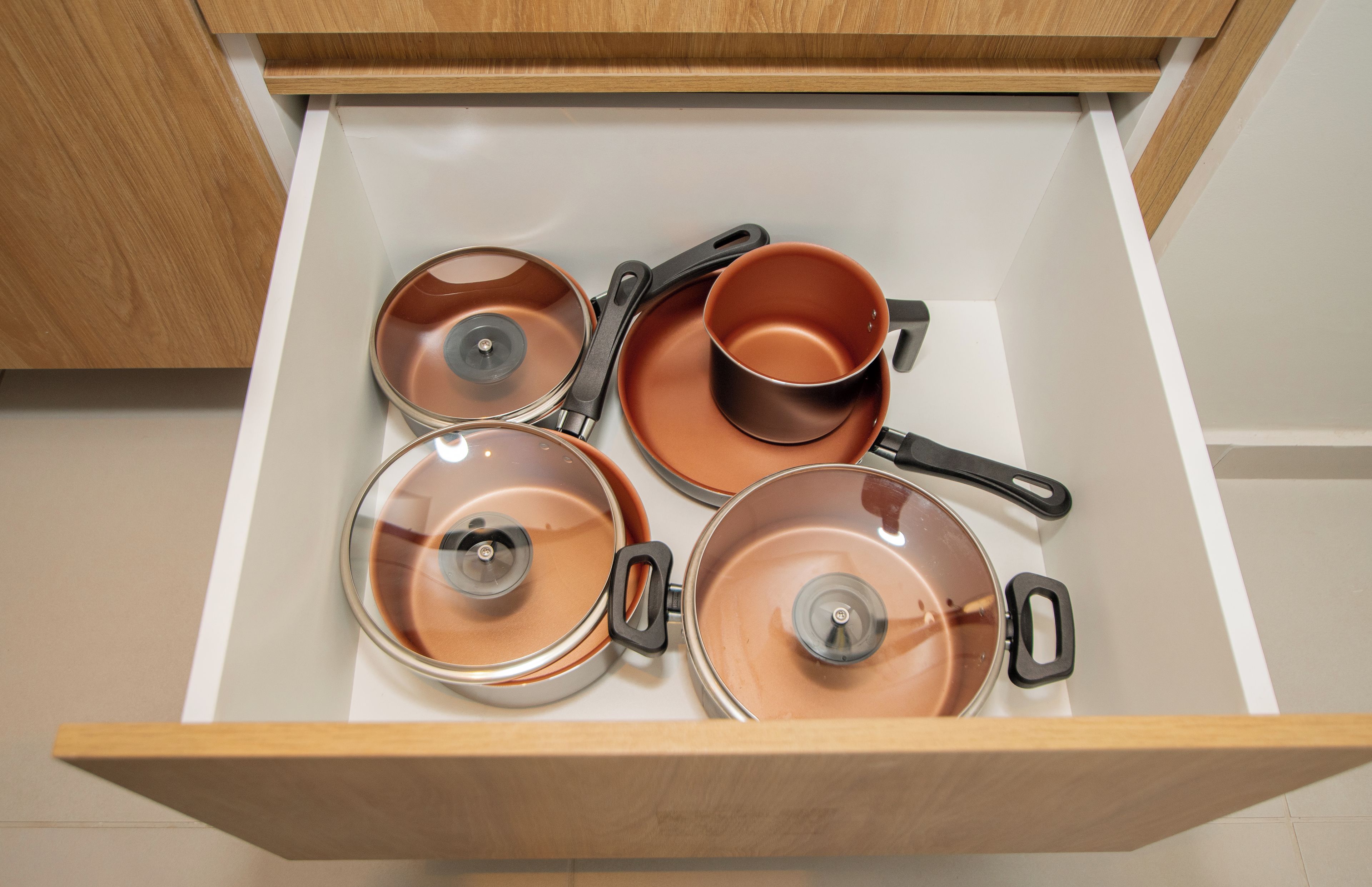 A drawer containing several copper-colored pots and pans.
